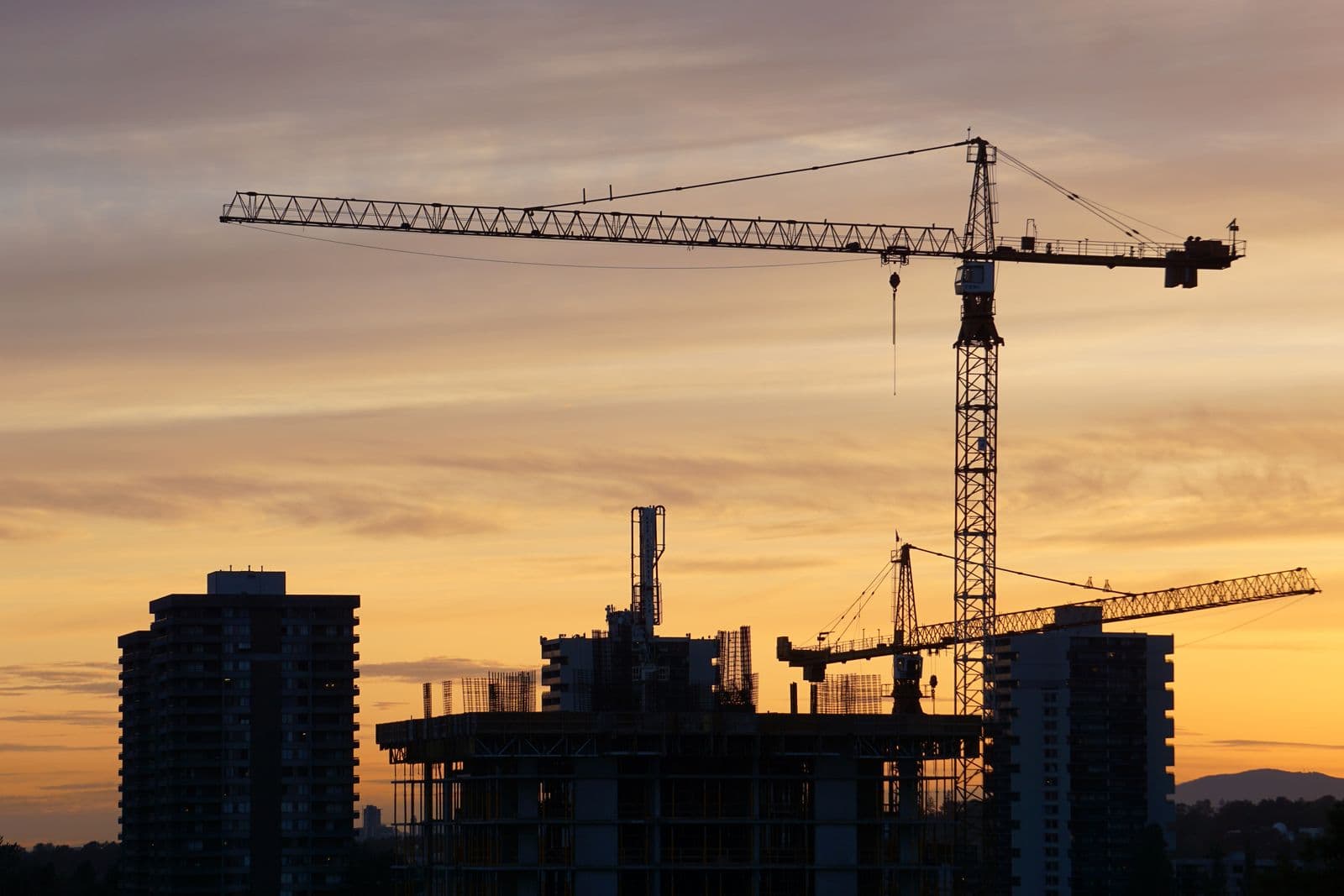 Tower cranes silhouetted over a partly built apartment block at sunset